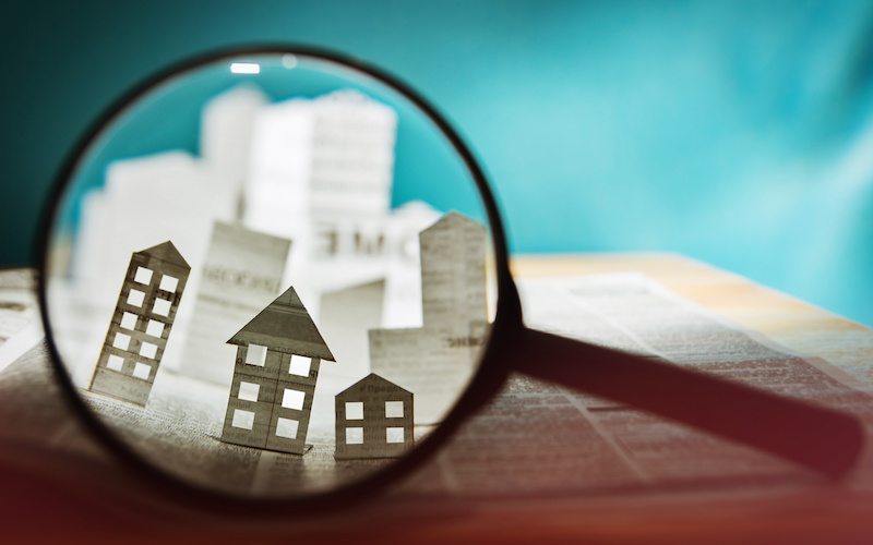 Magnifying glass in front of an open newspaper with paper houses.