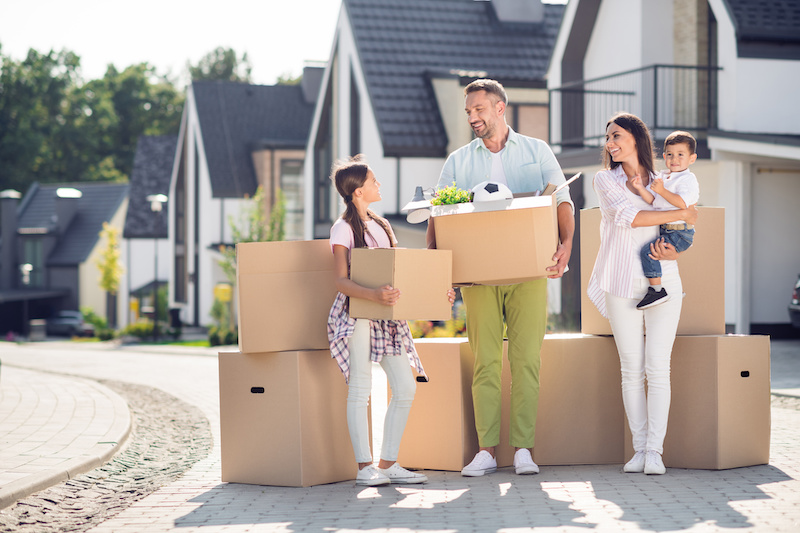 Full length body size view of four cheery people dad mom small little kids brother sister carrying cardboard boxes moving new residence cottage town.