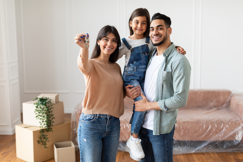 Portrait Of Happy Family Showing Key, Standing In Living Room. 