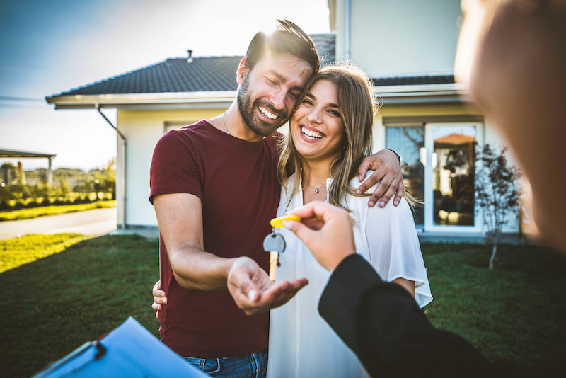 Happy millennial couple receiving keys from realtor, purchasing real estate