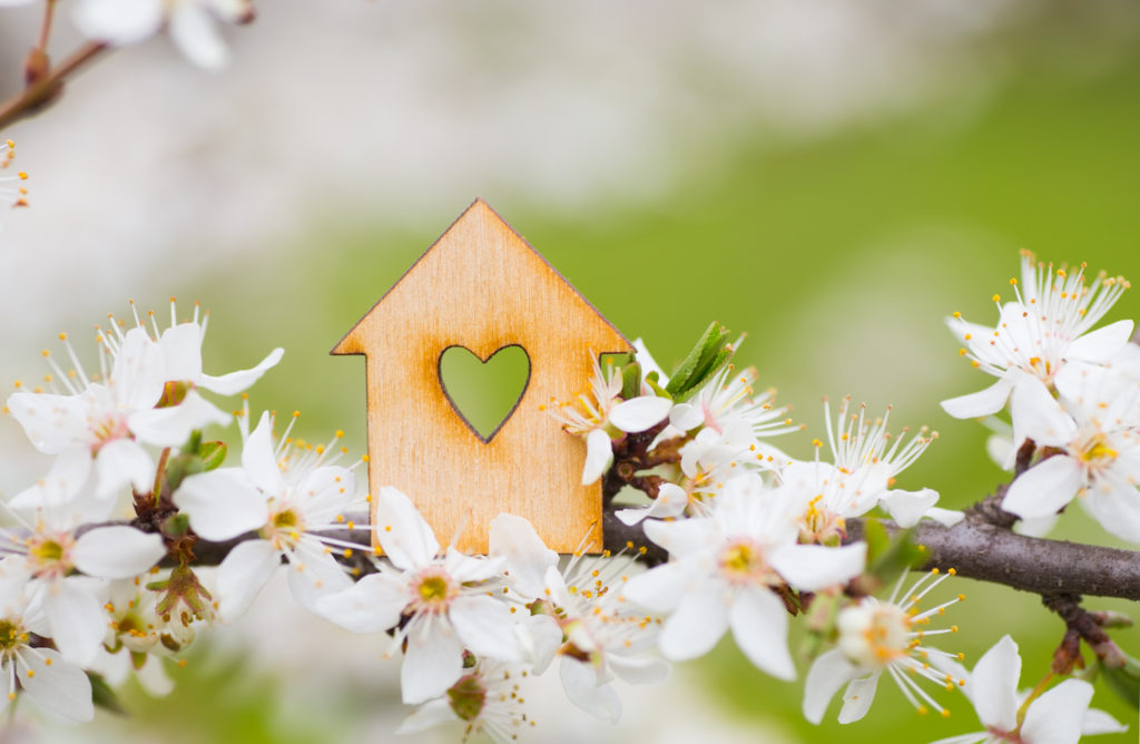 A small wooden house shape with a heart carved out surrounded by white flowers