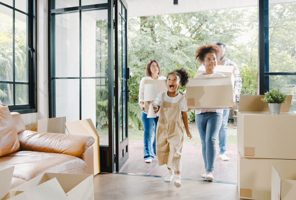 A young african american family moving into a new home carrying moving boxes